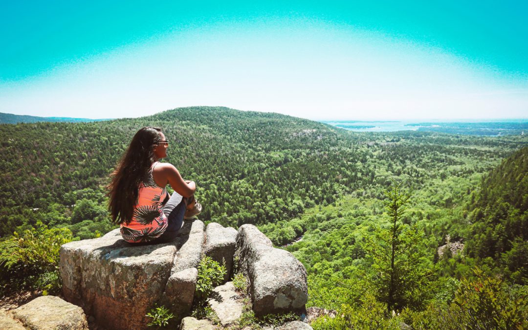Peaceful woman sitting on a rock cliff overlooking a lush forest
